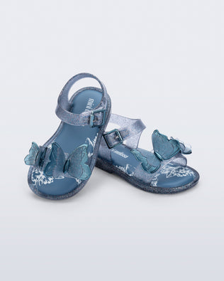 Angled view of a pair of glitter blue baby Butterfly sandals with blue butterflies