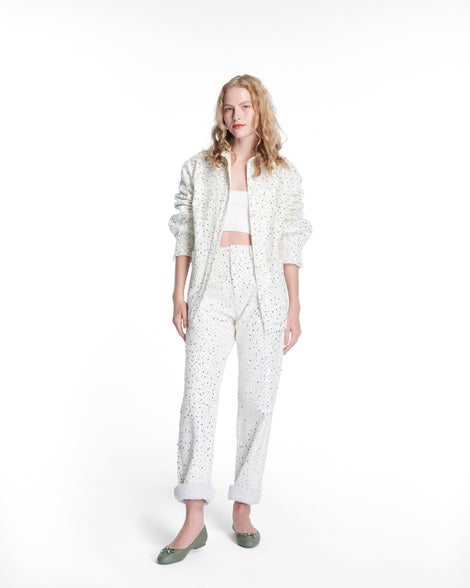 Model in a white jacket and pants wearing a pair of green Melissa flats with a bow detail with gold accents on the bow