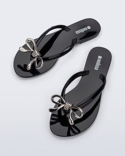 Top view of a pair of black Harmonic Iris flip flops with silver bow