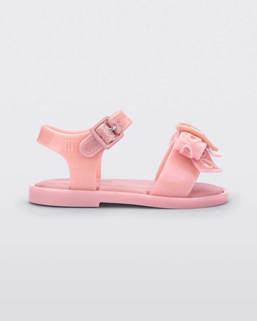 Side view of a glitter pink Mini Melissa Mar Sandal Heart sandal with a glitter pink heart bow detail on the front strap and an ankle strap