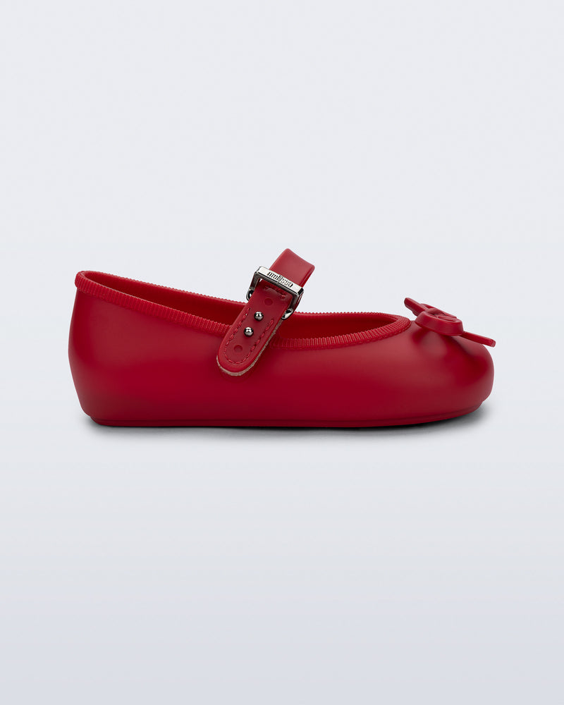 Side view of a red Soft Ballerina Delicate Bow baby  flat with top strap and bow