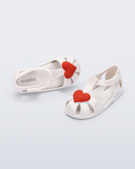 Side and top view of a pair of white Hip Heart Ballerina baby sandals with red heart on front