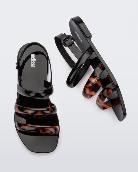 Side and top view of a pair of black and tortiose Essential Wave women's sandal with adjustable buckle.