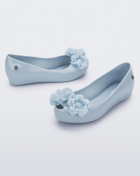 Angled view of a pair of a blue Ultragirl Springtime kids flat with two blue flowers and peep toe.