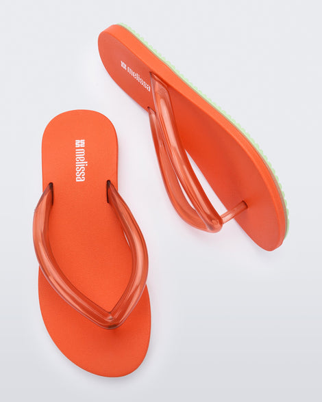 Top and side view a pair of orange Flip Flop Airflow sandals with a clear orange strap and green bottom
