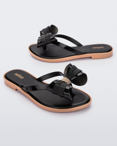 Angled view of a pair of Melissa slim strap flip flops in black with bow applique