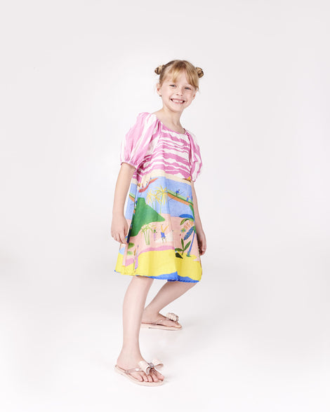 Model posing in a multi colored printed dress wearing a pair of Mini Melissa Flip Flops in pink with bow applique