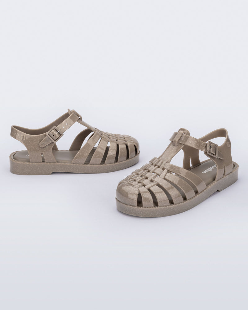 Side and angled view of a pair of glitter beige kids Possession fisherman style sandals.