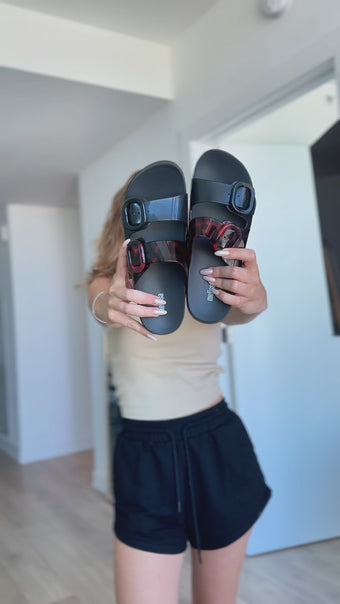 Influencer showing off the Melissa Cozy Slide Sandals in black tortoise color combo. The influencer is showing an outfit put together wearing the shoes. Her outfit also includes a leopard print maxi dress.
