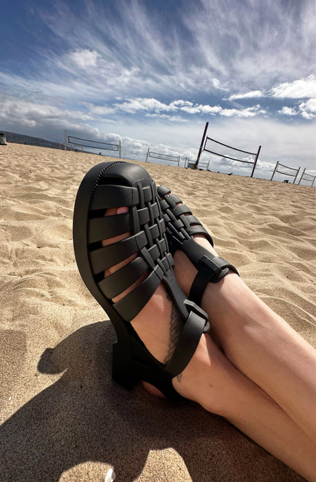 Model wearing the black matte possession sandals on a beach