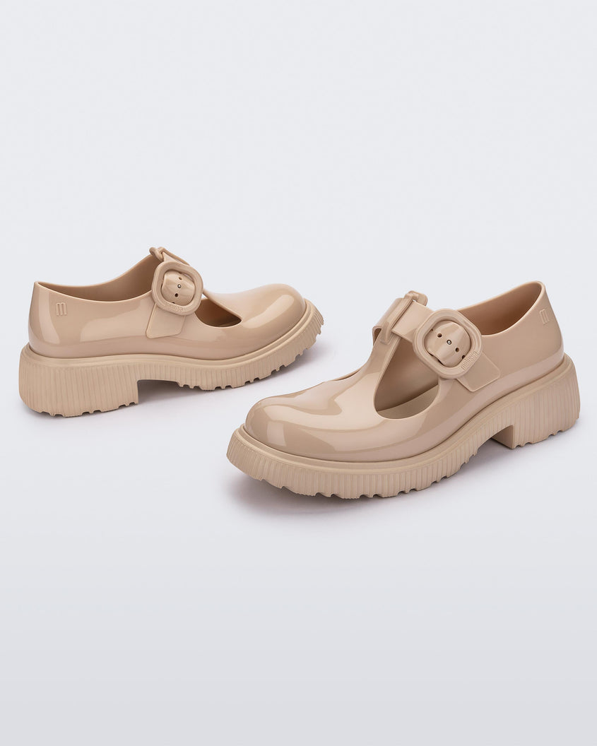 An angled side view of a pair of beige Melissa Jackie loafers with two cut outs and a buckle detail strap.