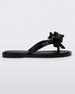 Side view of a Black Mini Melissa Slim flip flop with a lace like bow detail on the front straps.