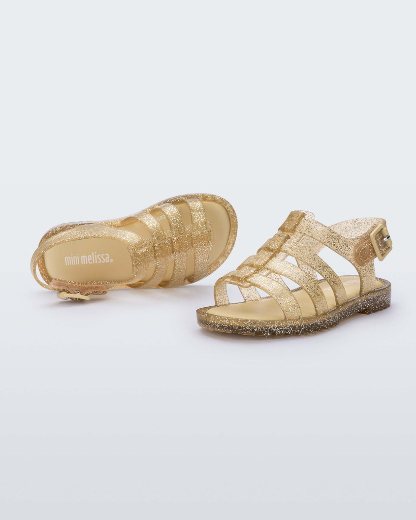 A top and side view of a pair of clear yellow glitter Mini Melissa Flox sandals with straps.