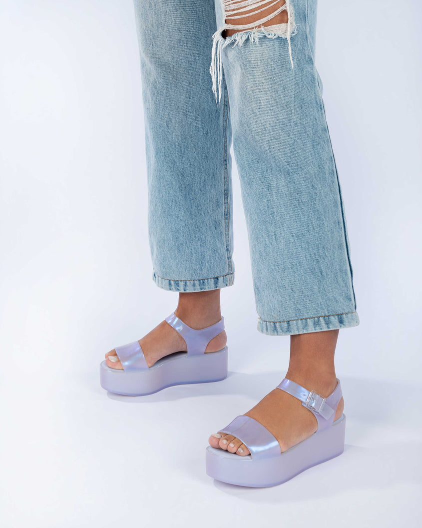 A model's legs wearing jeans and a pair of pearly blue Melissa Mar Platform sandals with two straps.