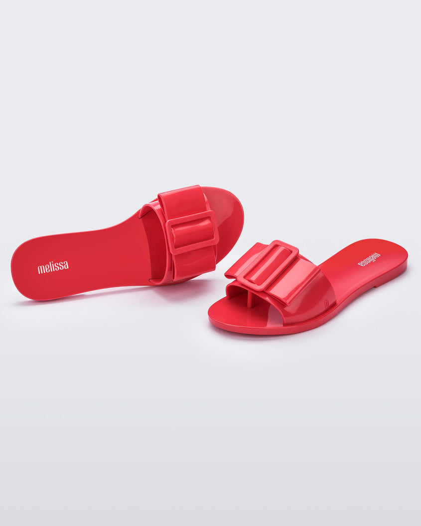 An angled front and top view of a pair of red Melissa Babe slides with a buckle like bow detail on the front strap.