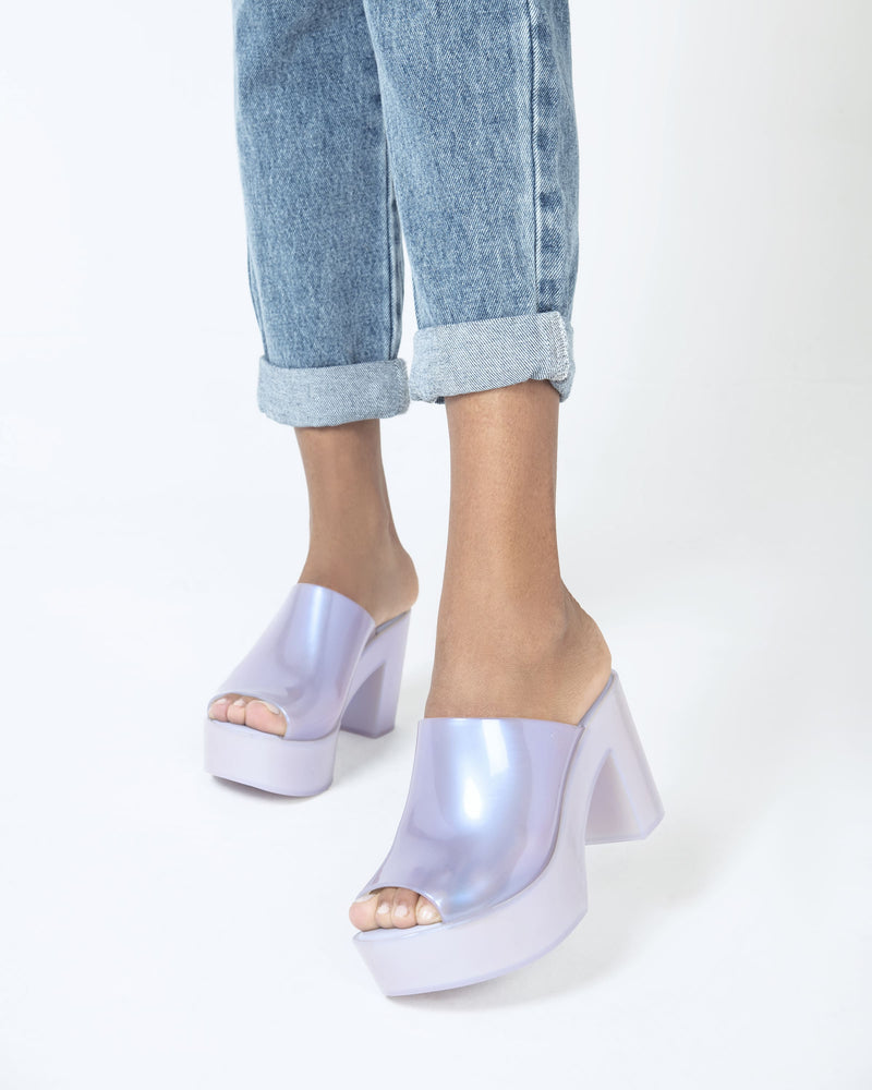 A model's legs wearing a pair of pearly white Melissa Mule plateform heels.