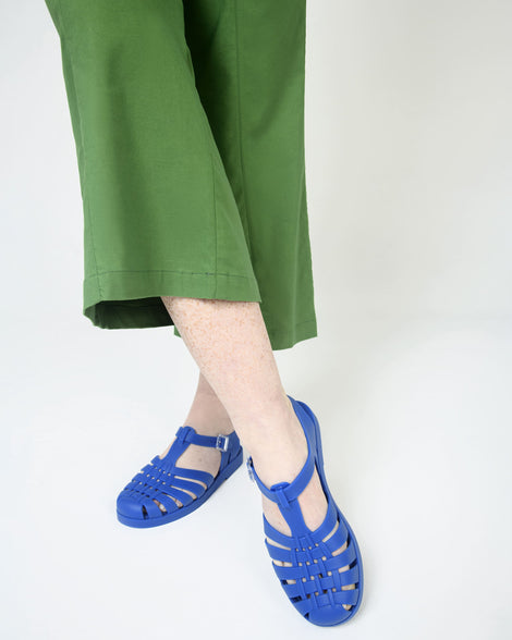Model's legs in green cropped pants wearing a pair of Melissa Possession fisherman sandals in blue, with cut out fishermen strap detail and clear buckle closure