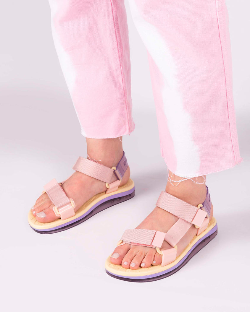 A model's legs wearing a pair of yellow soled Melissa Papete sandals with pink and purple straps.