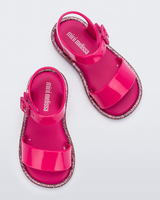 A top view of a pair of pink/pink glitter Mini Melissa sandals with two straps and a pink buckle.