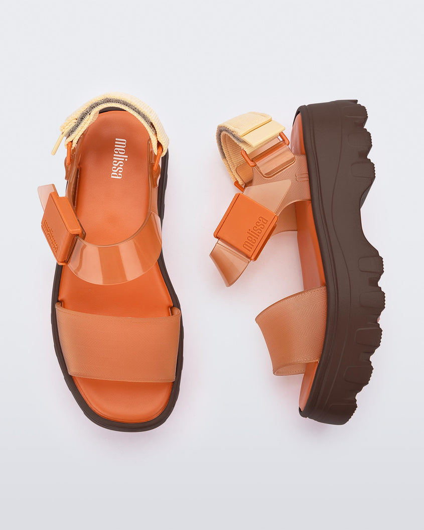 A top and side view of a pair of orange/clear orange platform Melissa Kick Off Sandals with two straps and a brown sole.