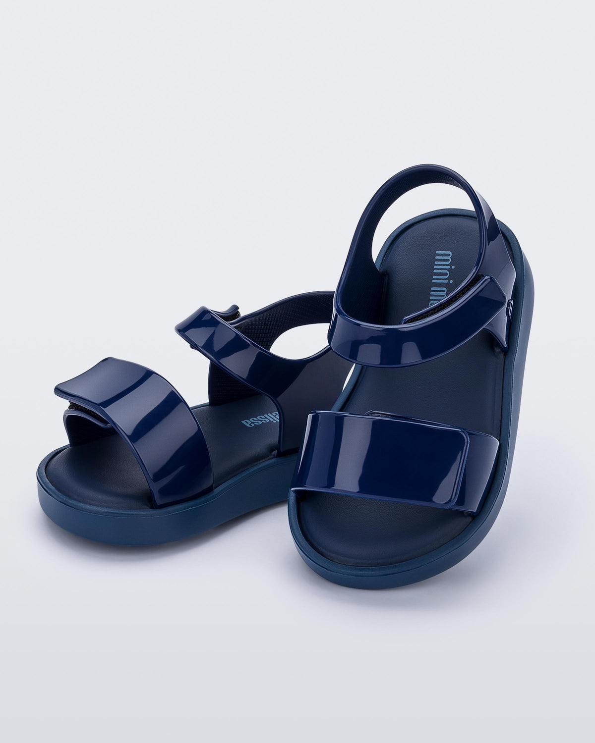 An angled side and top view of a pair of blue Mini Melissa Jump sandals with velcro straps.