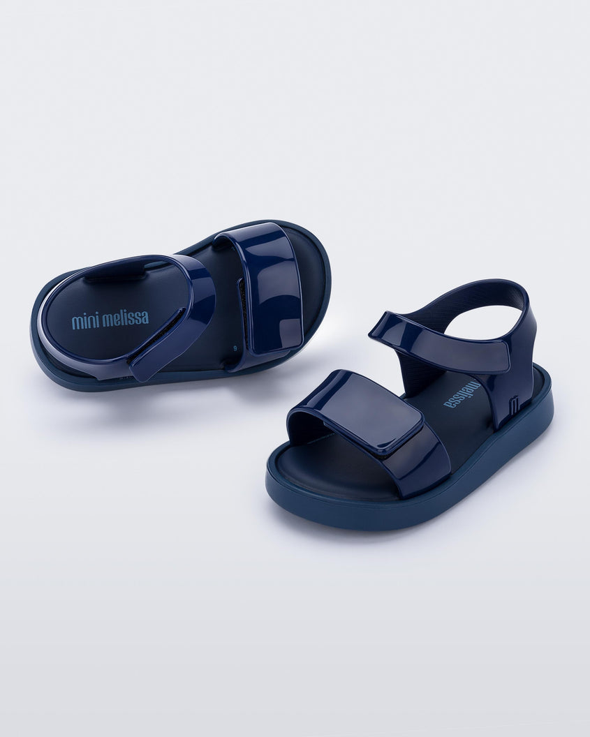 An angled top and side view of a pair of blue Mini Melissa Jump sandals with velcro straps.
