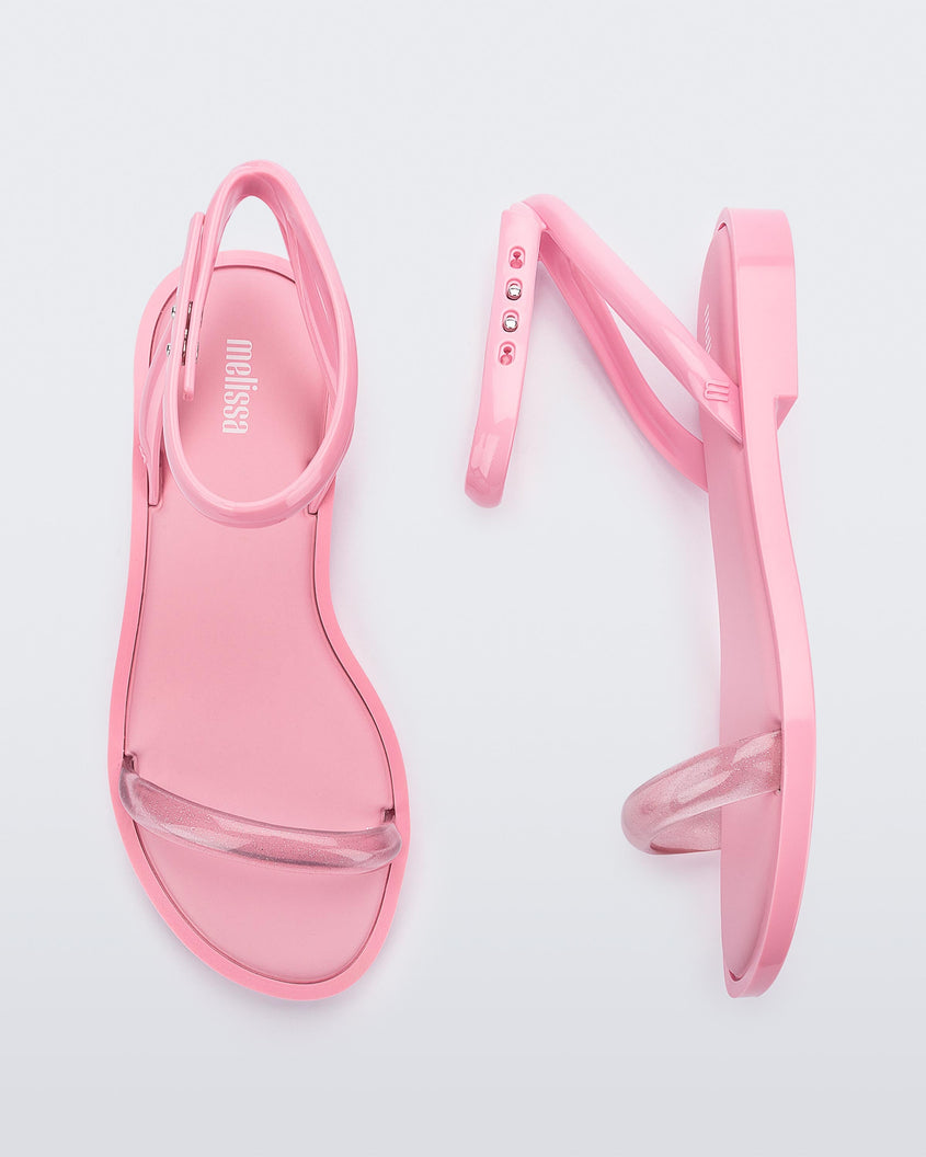 A side and top view of a pair of pink Melissa Wave Sandals with a clear pink front strap and a pink ankle strap and sole.