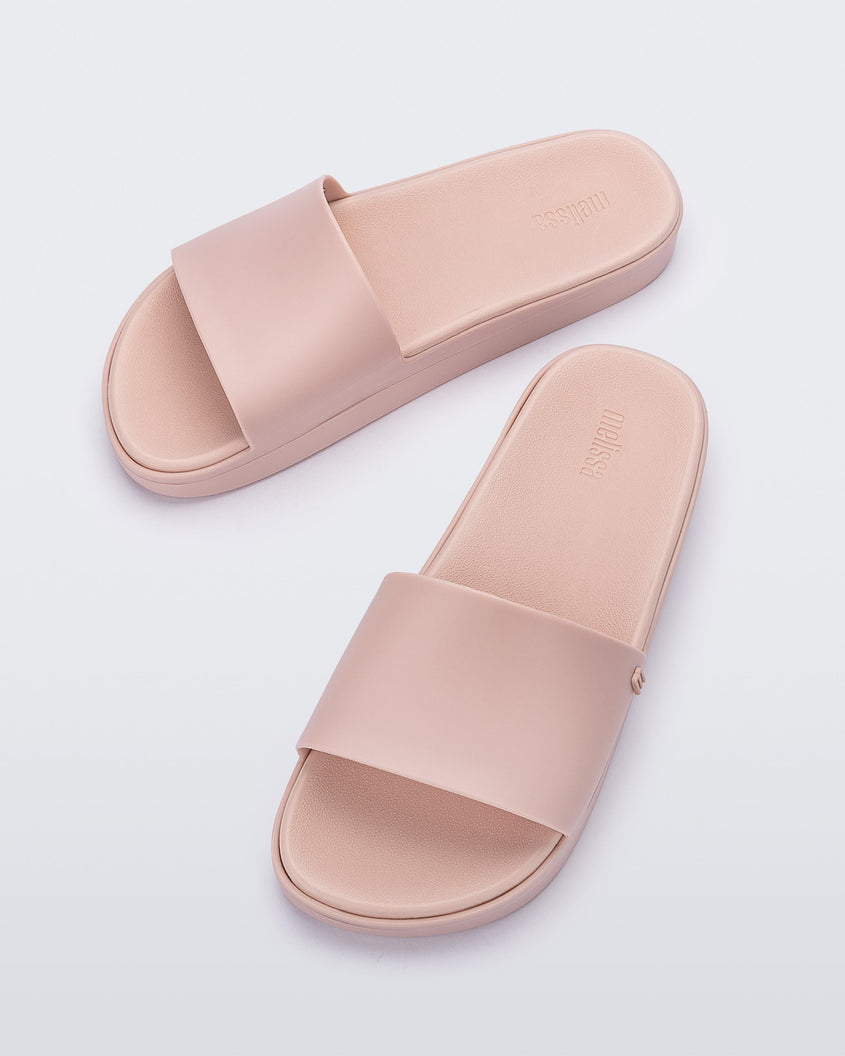 Angled view of a pair of light pink Melissa Beach slides. 