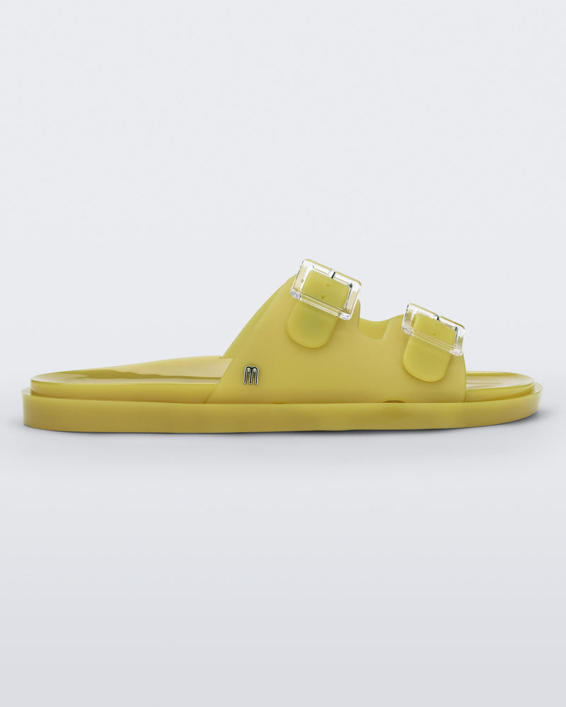 Side view of a yellow Melissa Wide Slide with two straps fastened on top with two clear buckles and a "m" logo on the side.