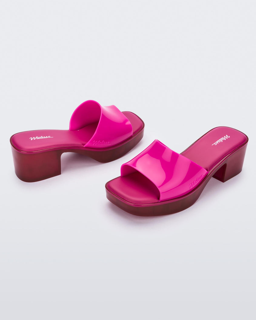 Angled view of a pair of Melissa Shape slides with transparent pink platform heel and a hot pink wide front strap. 
