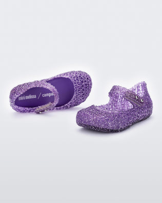 Top and angled view of a pair of Mini Melissa Campana purple glitter flats for baby with an open woven texture.