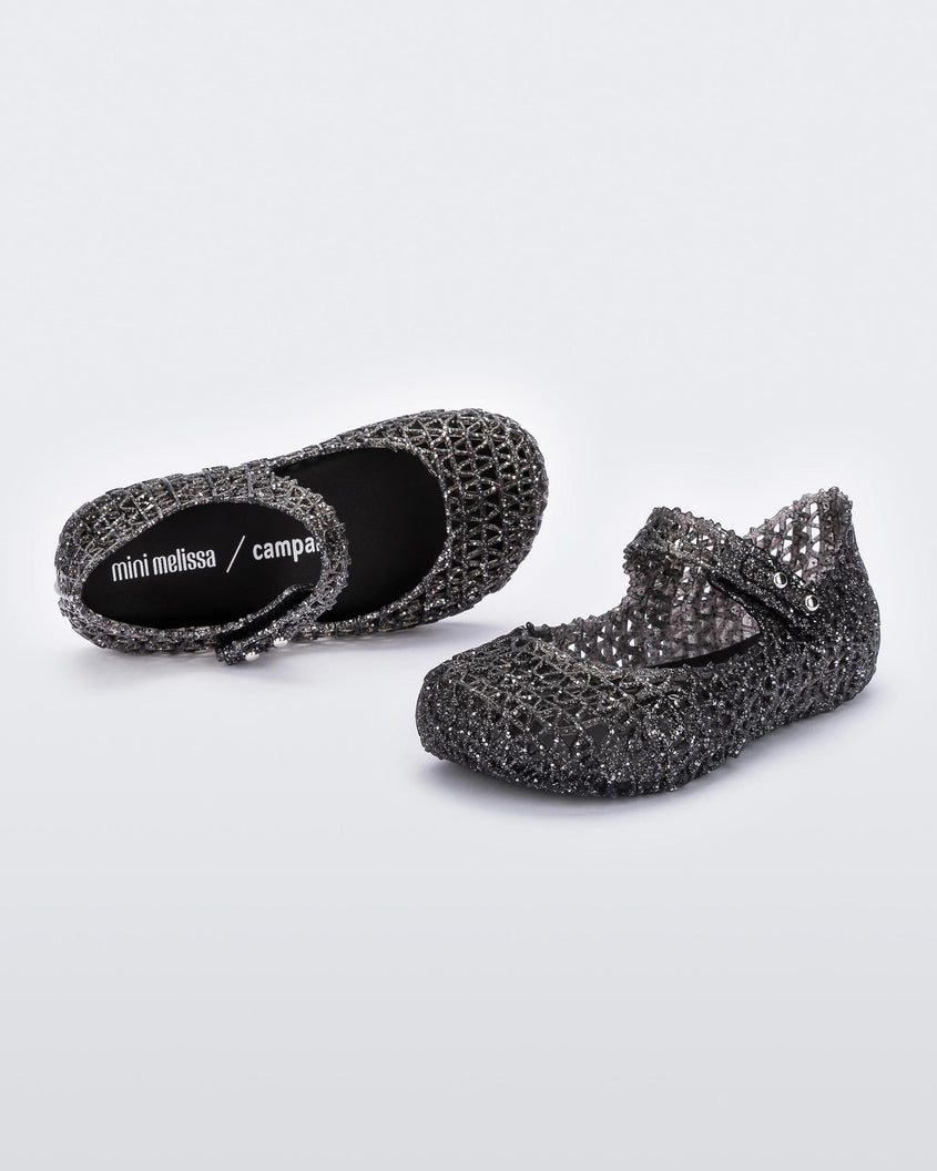 A pair of Mini Melissa Campana black glitter flats with a strap with snap closure for baby with an open woven texture