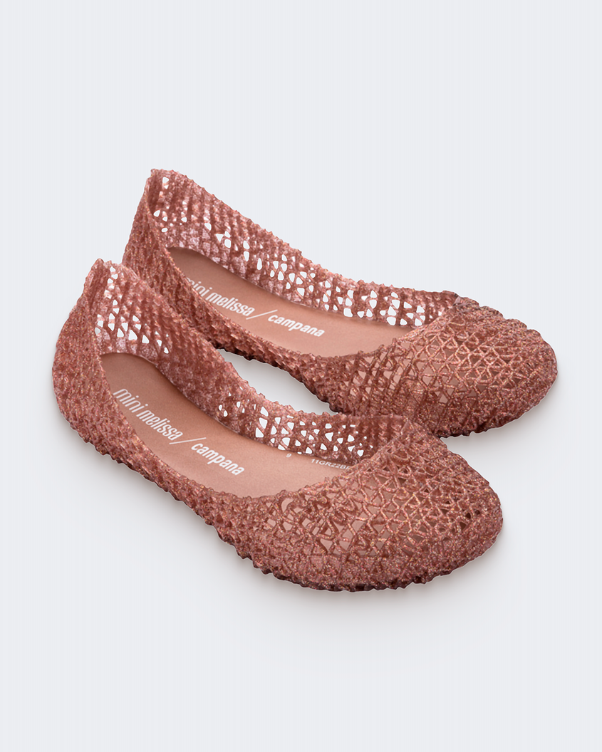 An angled top view of a pair of rose glitter Mini Melissa Campana flats with a woven detail base.