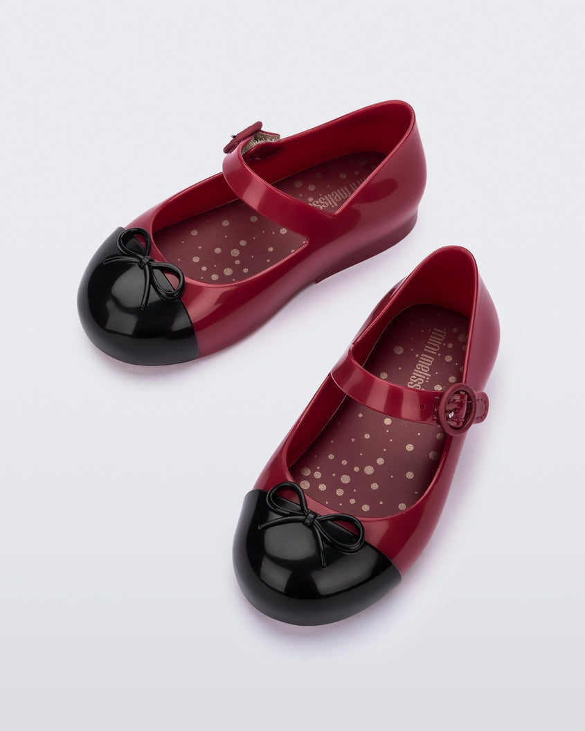 Top view of a pair of Red/Black Mini Melissa Sweet Love Cap Toe flats with a red base, top strap and a black toe cap with a bow detail on top.