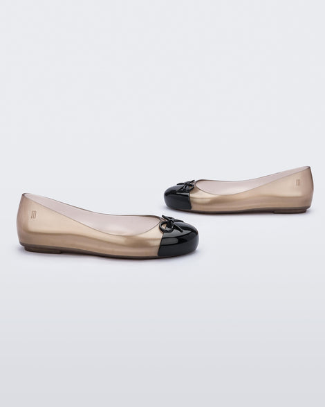 A side view of a pair of clear rose/black Mini Melissa Sweet Love Cap Toe flats with a clear rose base and a black toe cap with a bow on top.