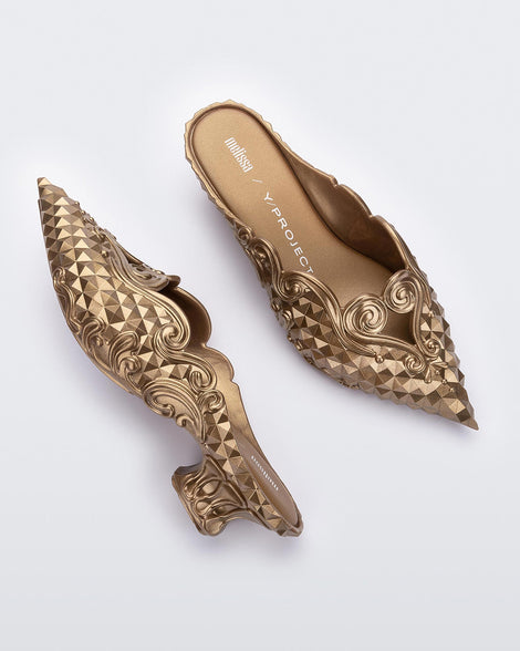A top and side view of a pair of metallic gold Melissa Court heels with a heart detail on the front and a checkered pattern texture.