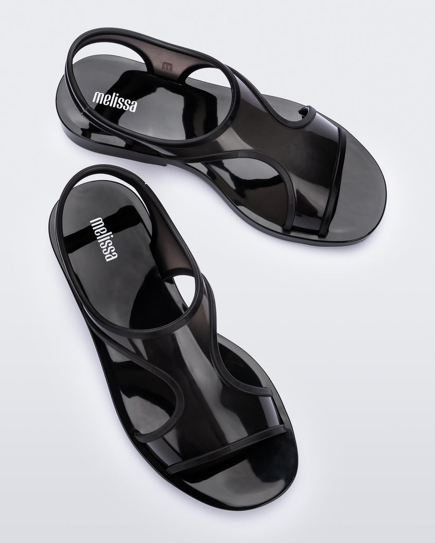 An angled top view of a pair of transparent black Melissa Bikini Sandals with two transparent black straps conjoining in the middle and a black insole.