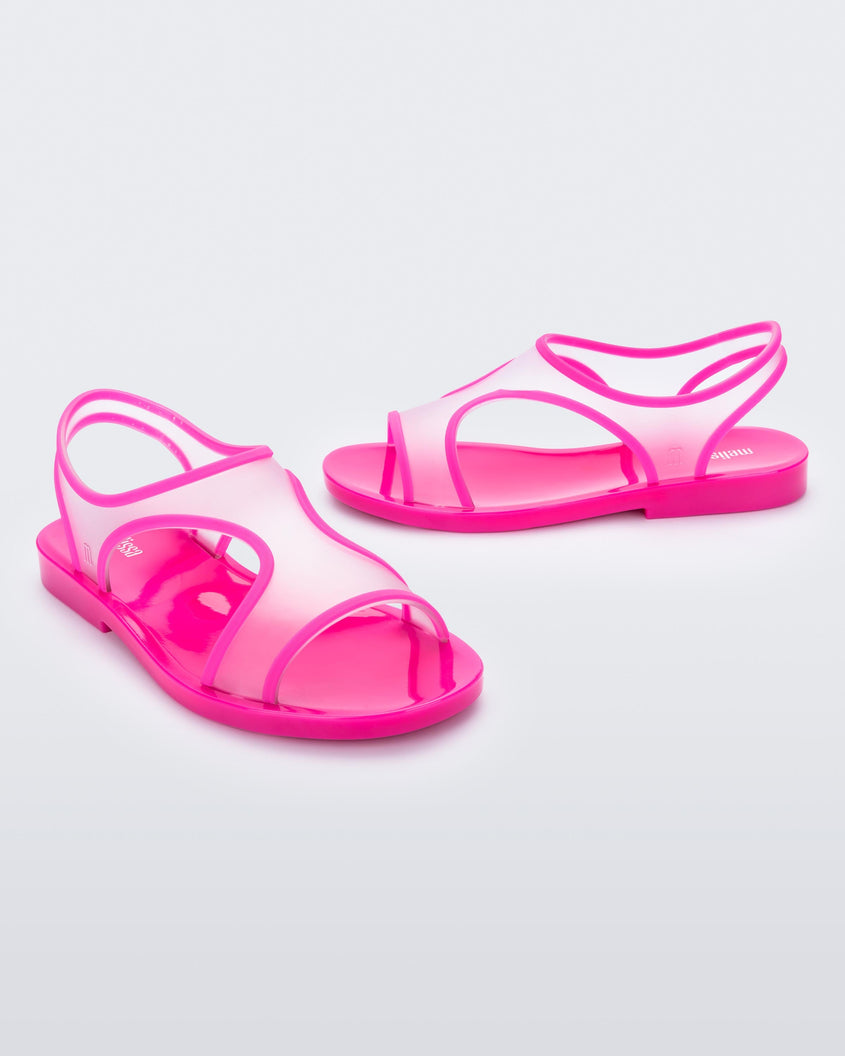 An angled front and side view of a pair of transparent neon pink Melissa Bikini Sandals with two transparent pink straps conjoining in the middle and a pink insole.