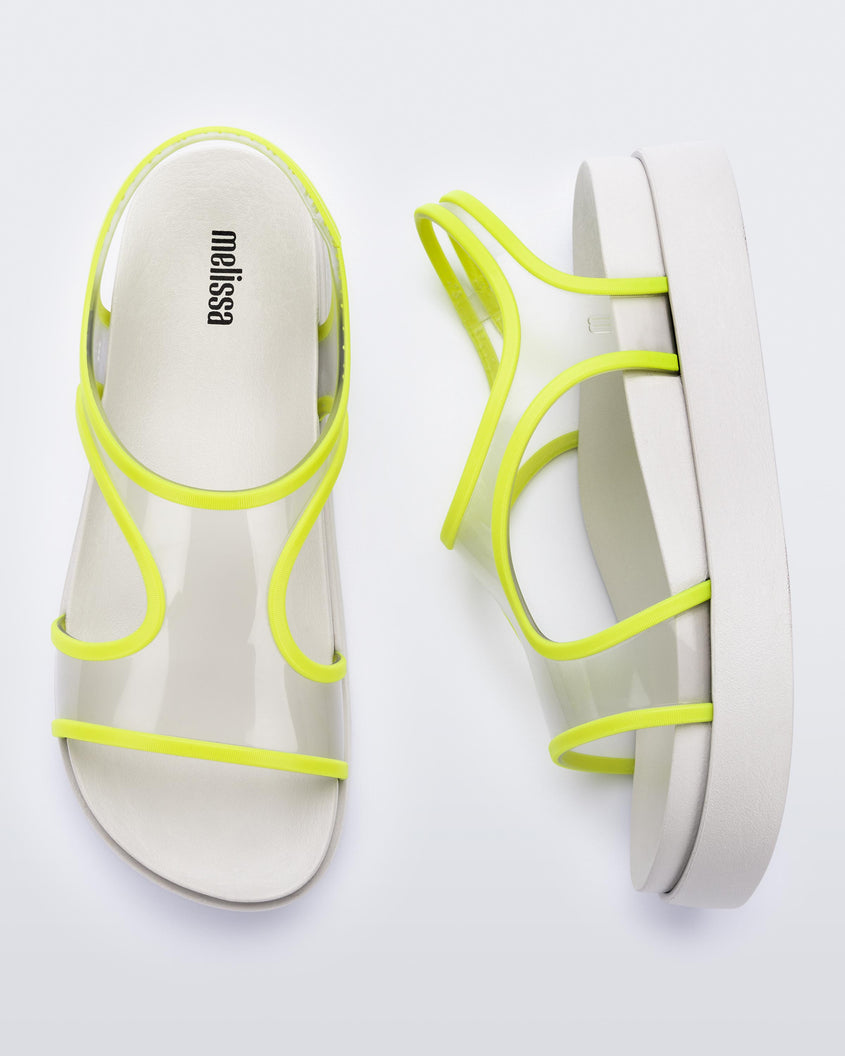 Top and side view of a pair of beige/green Melissa Bikini sandal with two transparent green straps conjoining in the middle and a beige insole.