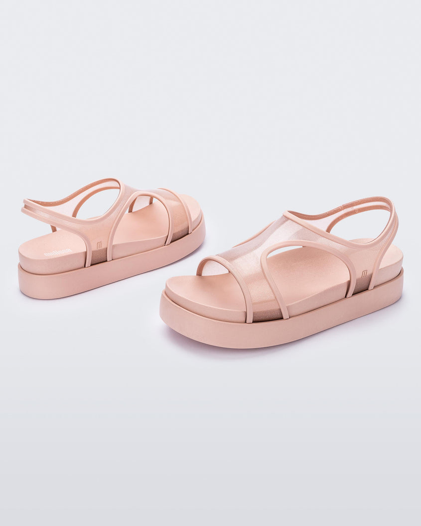 An angled side view of a pair of transparent pink glitter Melissa Bikini Platform sandals with two transparent pink glitter straps conjoining in the middle and a pink sole.