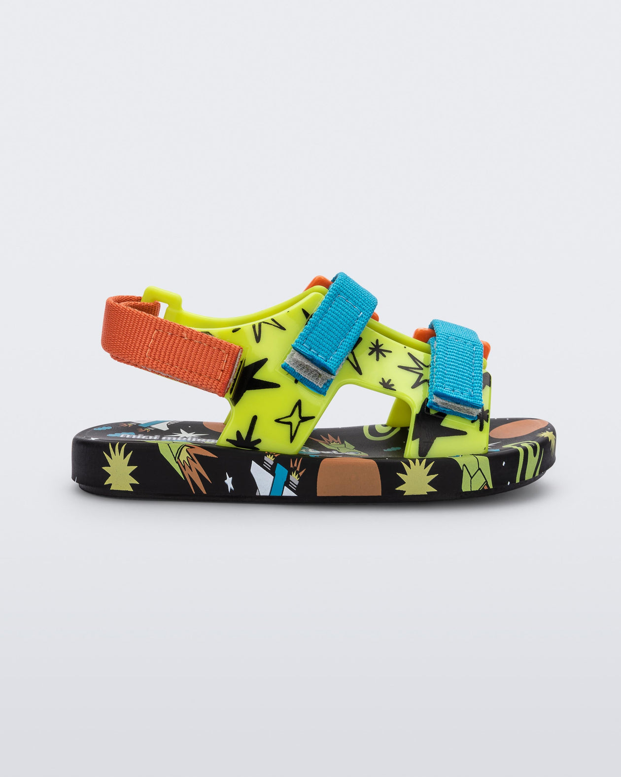 Side view of a black/green Mini Melissa Ping Pong sandal with a green patterned base, black patterned sole, two blue front velcro straps and and an orange back velcro strap.