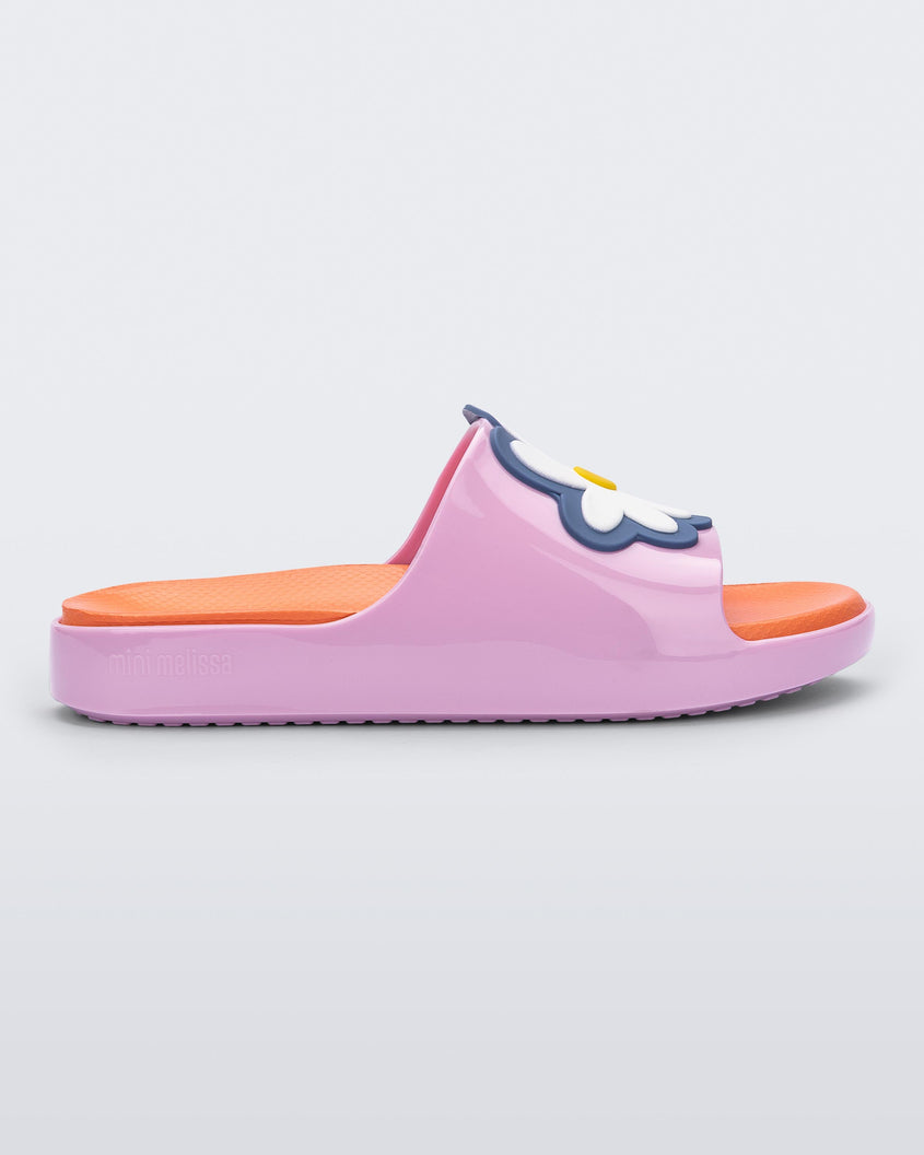 Side view of a pink/orange Mini Melissa Cloud slide with an orange insole, pink base and a flower detail on the front.