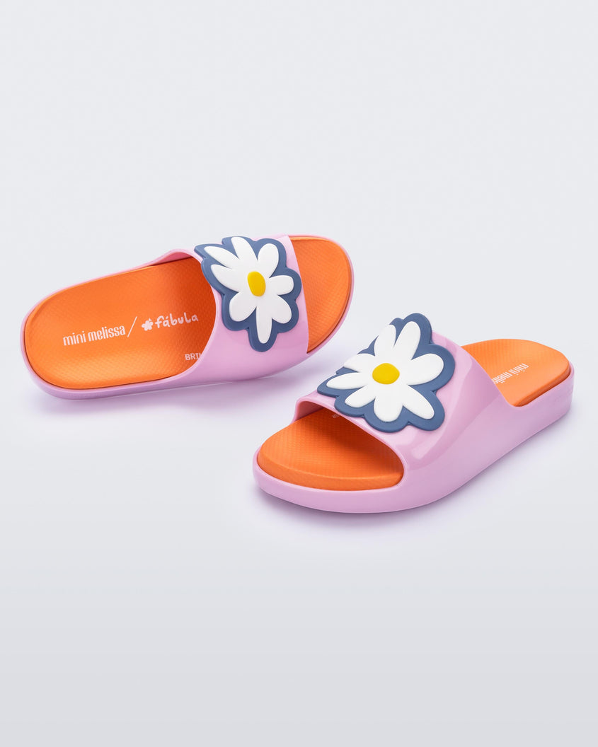 An angled top and side view of a pair of pink/orange Mini Melissa Cloud slides with an orange insole, pink base and a flower detail on the front.