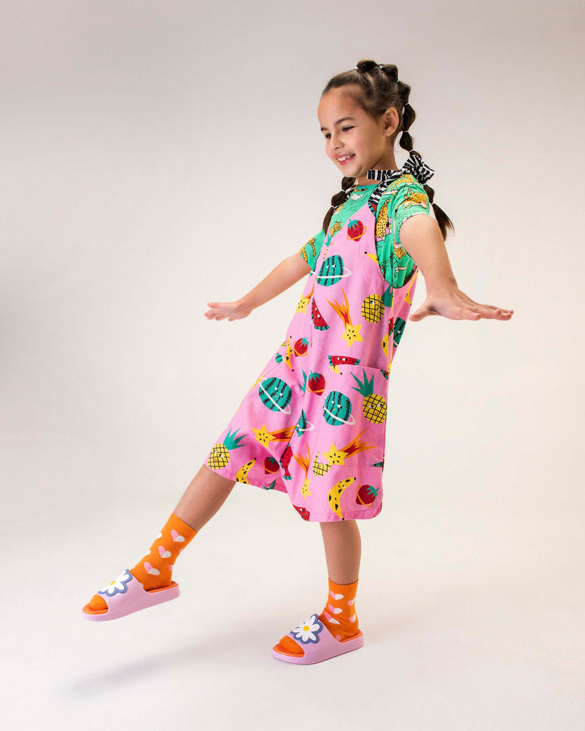 A model posing for a picture, in a pink dress, wearing a pair of pink/orange Mini Melissa Cloud slides with an orange insole, pink base and a flower detail on the front.