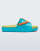A child's blue slide sandal with an green insole and a multicolored character illustration on the strap.