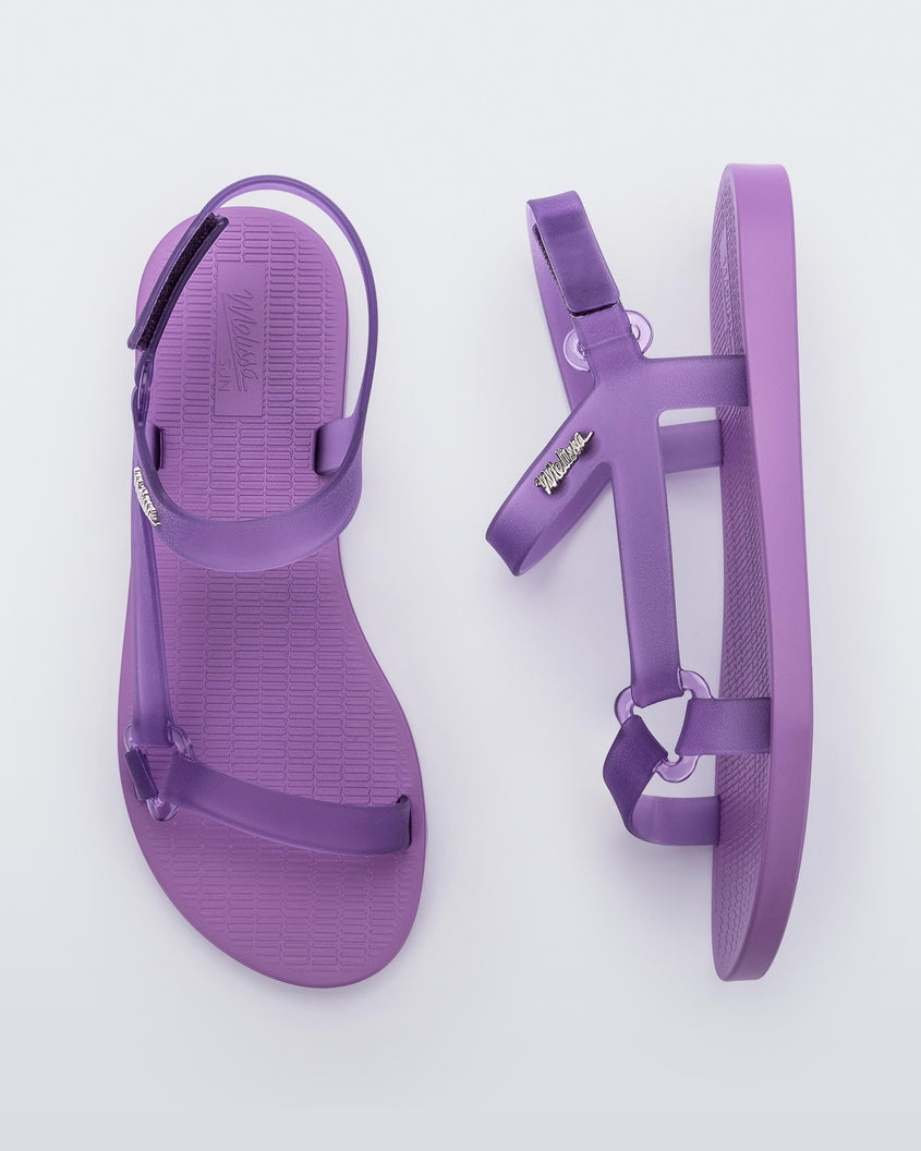 Top and side view of a pair of Melissa Sun Downtown sandals with transparent lilac front cross and back ankle straps and a lilac purple sole. 