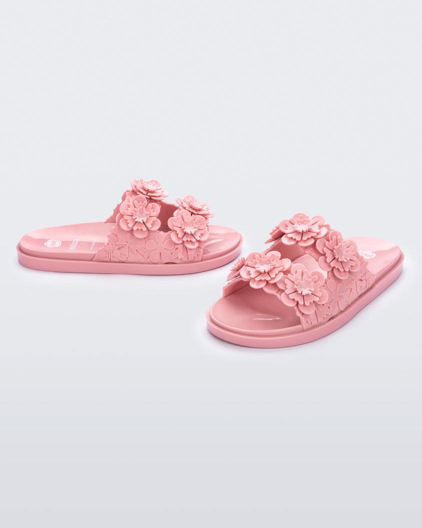 Angled view of a pair of Melissa Wide Blossom Slides in pink with double floral embossed buckle straps and 3D flower appliques