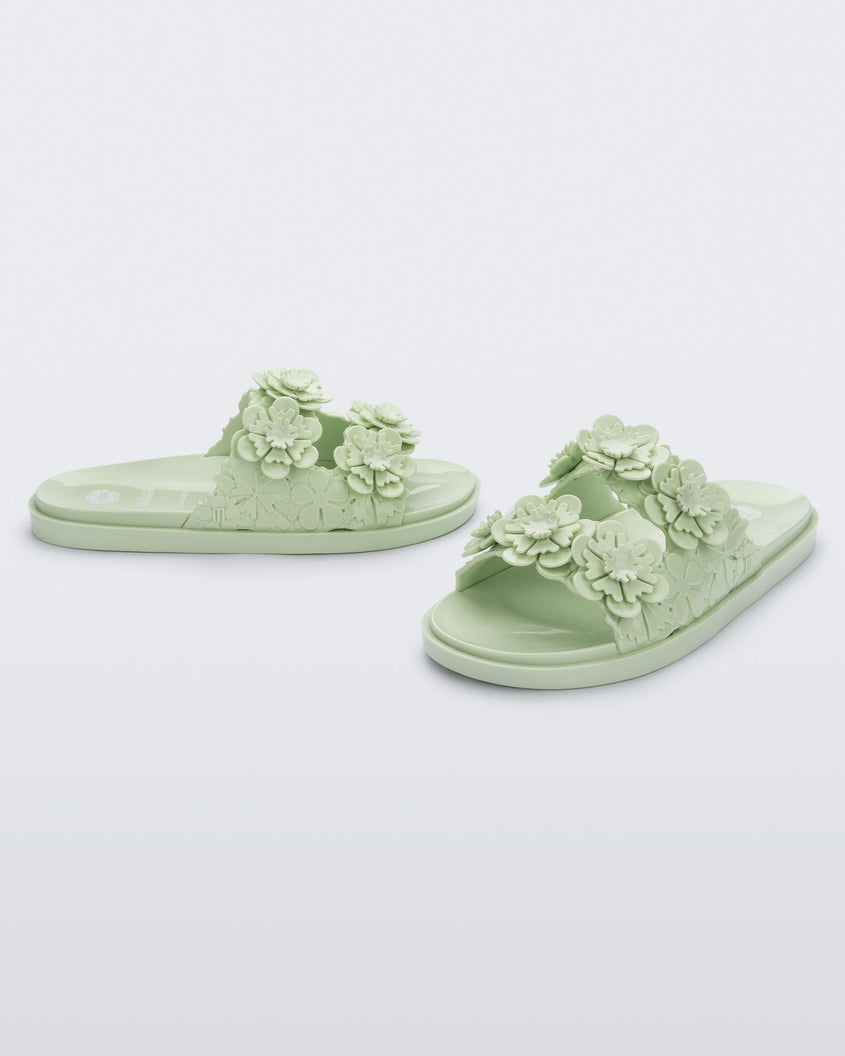 Angled view of a pair of Melissa Wide Blossom Slides in green with double floral embossed buckle straps and 3D flower appliques