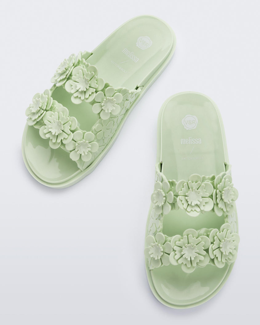Top view of a pair of Melissa Wide Blossom Slides in green with double floral embossed buckle straps and 3D flower appliques