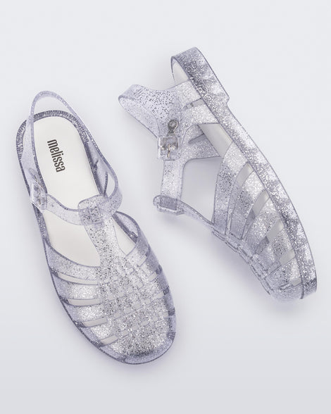 An top and side view of a pair of glitter clear Melissa Possession sandals with several straps and a closed toe front.